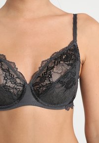 Sujetador de encaje negro y tela gris con un escote pronunciado, que presenta delicados patrones florales y tirantes ajustables.
