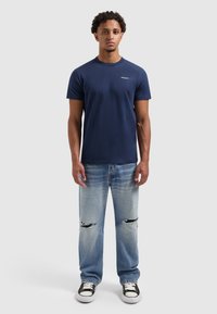 Navyblauwe katoenen T-shirt met korte mouwen en een ronde hals, gecombineerd met lichtblauwe distressed jeans met zichtbare scheuren en zwarte sneakers.