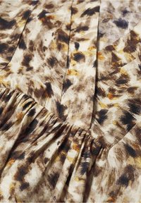 Tissu avec couture froncée et motif animal abstrait en tons beige, marron, noir et jaune.
