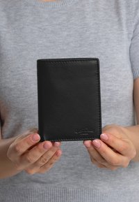 Black leather wallet with a smooth texture, rectangular shape, and subtle stitching. Features embossed logo at the bottom.