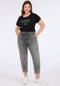 Musta puuvillapaita, jossa on valkoista tekstiä ja hengarigrafiikkaa, yhdistettynä haalistuneisiin harmaisiin farkkuihin, joissa on koristeluita ja käännetyt lahkeet. Valkoiset lenkkarit.