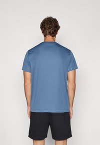 Blå kortærmet trænings t-shirt lavet af glat stof, med rund hals og et enkelt design, parret med sorte shorts.