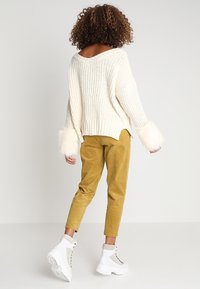 Pull en tricot crème avec des poignets duveteux, assorti à un pantalon en velours côtelé moutarde et des bottines blanches à grosses semelles.