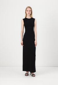 Svart ermeløs maxikjole med en tettsittende silhuett. Glatt stoff, høy halslinje og gulvlengde design. Svart hæl Sandaler med blomsterdetaljer.