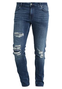 Jeans de mezclilla azul con un corte ajustado, que presentan áreas desgastadas y detalles rasgados en las rodillas. Diseño clásico de cinco bolsillos y cremallera.