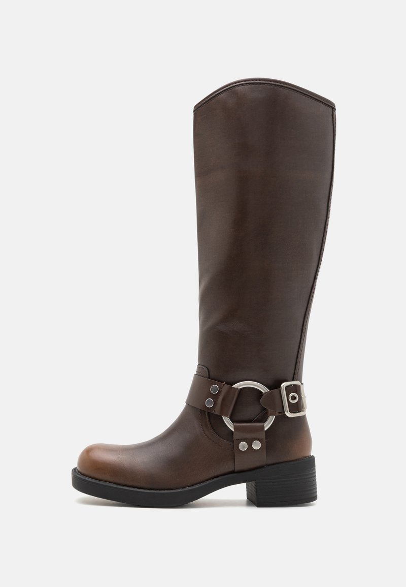 Bota de cuero marrón hasta la rodilla con un acento de hardware metálico redondo y hebilla. Parte superior ligeramente texturada, tacón apilado y diseño de punta redondeada.