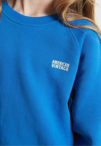 Helles blaues Sweatshirt aus weichem Stoff mit geripptem Kragen und Bündchen. Mit weißem "AMERICAN VINTAGE" Logo auf der Brust.