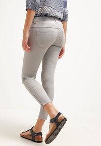 Pantaloni slim-fit grigio chiaro con tasche posteriori, abbinati a sandali neri con suole in sughero e cinghie regolabili.