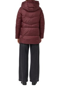 Bordeauxrode gewatteerde jas met capuchon, voorzien van doorgestikte vlakken en een licht getailleerde taille. Gecombineerd met wijde donkergrijze broekspijpen en zwarte laarzen.
