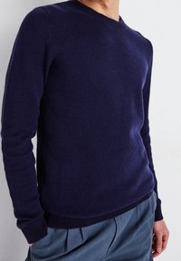 Marinblå stickad tröja med texturerad tyg, rund halsringning och ribbad nederkant och ärmslut. Matchas med ljusblå byxor.