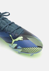 Scarpa da calcio Puma con tomaia blu scuro, design a strisce blu e verde, superficie texturizzata e chiusura con lacci, dotata di suola verde.