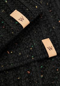 Czarna dziergana czapka z kolorowymi kropeczkami. Posiada jasnobrązową skórzaną metkę z literą "W". Teksturowany wzór o grubym, przytulnym wyglądzie.