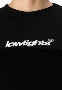 Black t-shirt with a round neckline, featuring white embroidered text "lowlights®" prominently displayed on the chest.