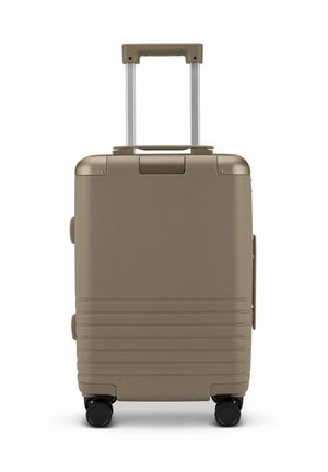 Valise rigide beige avec une poignée extensible et quatre roues noires, posée verticalement sur un fond blanc.