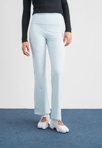 Svetlomodré jogínske nohavice so širokým pásom, vyrobené z hladkej, elastickej látky. Logo Nike na ľavom bedri. Nosia sa s bielymi športovými topánkami.