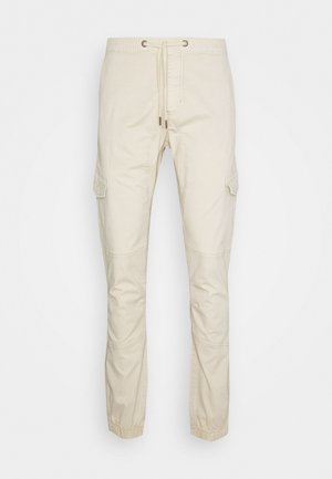 Beige cargo pants made of soft cotton, featuring a drawstring waist, side pockets, and elasticized cuffs. Smooth texture with tailored design.