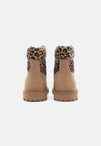 Bottes en suède beige avec un col en fourrure imprimé léopard, présentant une semelle extérieure texturée et un bout rond. La hauteur du talon est d'environ 2,5 cm.