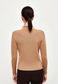 Langärmliger, brauner gerippter Rollkragenpullover mit taillierter Passform, glatter Textur und kleinem Kragen, kombiniert mit dunklen Hosen.