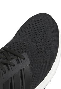 Close-up of black knit running shoe with black laces and white cushioned sole.