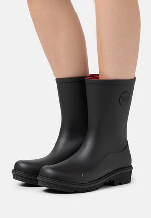 Black rubber rain boots with smooth finish, red interior lining, and textured black sole, featuring a circular logo on the outer side.