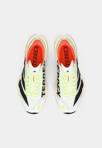 Λευκά και μαύρα αθλητικά παπούτσια με κίτρινες λεπτομέρειες, επάνω μέρος από υφή δικτυωτού υφάσματος, πράσινα κορδόνια και πορτοκαλί εσωτερική επένδυση, με το λογότυπο "TERREX".