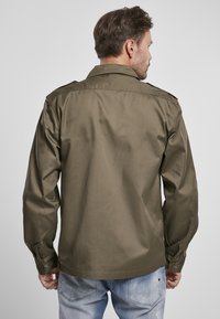 Camisa de manga larga verde oliva con cuello plano, puños abotonados y una textura suave. Presenta hombreras y un corte entallado.