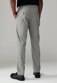 Pantalons gris en tissu texturé, avec des poches arrière à boutons, accompagnés de chaussures noires.