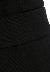 Zwarte stoffen legging met een gladde textuur, voorzien van een hoge tailleband en subtiele stiksels langs de bovenkant voor een getailleerde pasvorm.