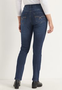 Mörkblå denimjeans med hög midja, slim fit och sydda bakfickor med ett accentmönster. Slät textur och ren finish.