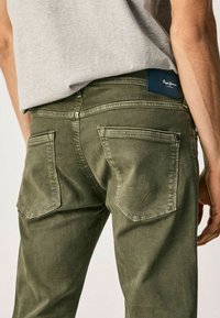 Pantaloni in denim verde oliva con vestibilità slim. Presentano due tasche posteriori con dettagli di cucitura e un'etichetta blu del brand sulla vita.