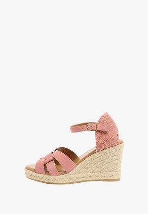 Roze suède sleehaksandaal met gevlochten hak, enkelriem en open teen in zijaanzicht op een witte achtergrond.