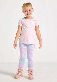 Svetloružová košeľa s krátkym rukávom s kvetinovou výšivkou; legíny s pastelovým vzorom v ružovej a modrej farbe; béžové členkové topánky.