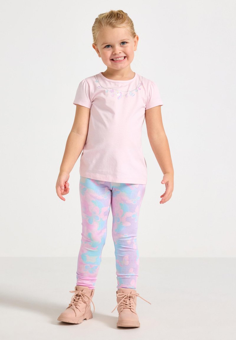 Svetloružová košeľa s krátkym rukávom s kvetinovou výšivkou; legíny s pastelovým vzorom v ružovej a modrej farbe; béžové členkové topánky.