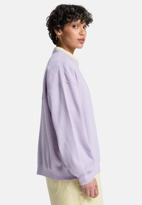 Ανοιχτό μοβ φούτερ με χαλαρή εφαρμογή, ριμπ μανσέτες και στρογγυλή λαιμόκοψη. Διαθέτει μικρό σχέδιο στον αριστερό ώμο.