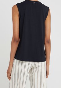 Haut sans manches navy en tissu doux, avec un col rond et un petit logo au dos, associé à un pantalon rayé.