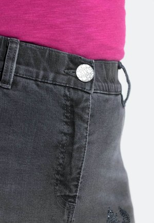 Szare dżinsowe spodnie z srebrnym guzikiem z napisem oraz kontrastujący różowy top. Tkanina jest gładka z delikatnym połyskiem.