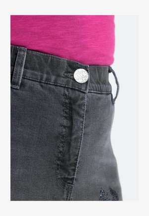 Pantaloni di denim grigio con un bottone argento con testo, e una maglietta rosa a contrasto. Il tessuto è liscio con una leggera lucentezza.