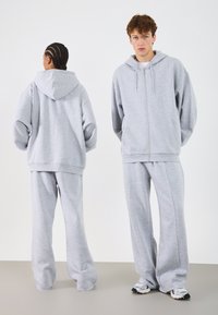 Hall kaelusega zip-up kapuutsiga ja sobivad dressipüksid. Pehme, mugavalt lõtv kangas. Mudel on näidatud eest ja tagant.