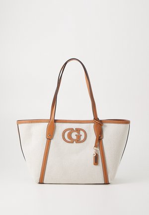 Sac fourre-tout en toile beige avec garniture en cuir marron clair, poignées doubles, patch logo décoratif et un petit charme suspendu sur le côté avant droit.