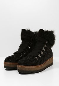 Botas negras hasta el tobillo con adornos brillantes,cordones en la parte delantera y ribete de piel sintética, montadas sobre una suela gruesa y texturizada.
