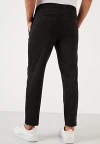 Tmavě šedé texturované kalhoty s úzkým střihem, zadními kapsami a elastickým pasem, v kombinaci s bílými teniskami.