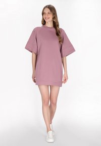 Przesadzona sukienka swetrowa w odcieniu mauve, z krótkimi rękawami, okrągłym dekoltem i prostym dołem. Stylizowana z białymi sneakersami.
