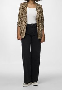 Blazer s leopardím potiskem přes bílý top s ramínky, v kombinaci s černými džínami s vysokým pasem a černými teniskami. Tkanina vypadá hladce a má volný střih.