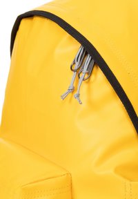Mochila amarilla con una superficie brillante y resistente al agua. Presenta un zipper negro con tiradores plateados y acentos de cordón gris. Diseño simple y moderno.