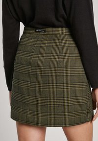 Green plaid skirt features a fitted waist, soft fabric, and subtle pleats. The pattern includes dark and light stripes with a raw hem.