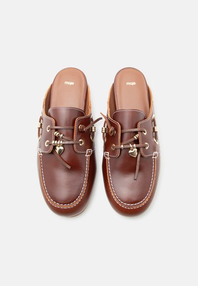 Καφέ δερμάτινα μοκασίνια χωρίς κορδόνια με λευκή ραφή, διακοσμητικά κορδόνια, χρυσές χάντρες και καρδιοειδείς γοητείες, με την επωνυμία "moje" στο εσωτερικό.