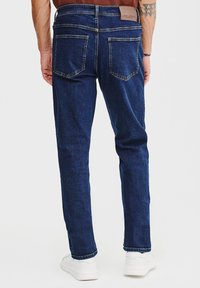 Granatowe dżinsy o prostym kroju, pięć kieszeni, skórzana naszywka z brandingiem w talii oraz subtelne detale przeszycia.