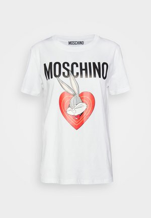 Nainen pukeutuneena valkoiseen Moschino-t-paitaan, jossa Bugs Bunny -kuvio, punaiseen hameeseen, jossa isot napit, mustiin läpikuultaviin sukkiin ja mustiin loafer-kenkiin.