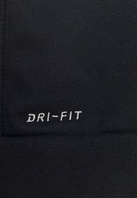 Tela negra texturizada con el texto bordado en blanco "DRI-FIT" cerca de la costura.