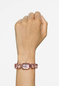 Reloj rectangular rosa con una correa transparente y facetada. La carátula tiene tres agujas y una pequeña esfera. Los toques metálicos brillantes realzan el diseño.